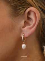 Three sizes of gold pavé waterproof hoop earrings with natural freshwater pearl drops displayed on a textured neutral background