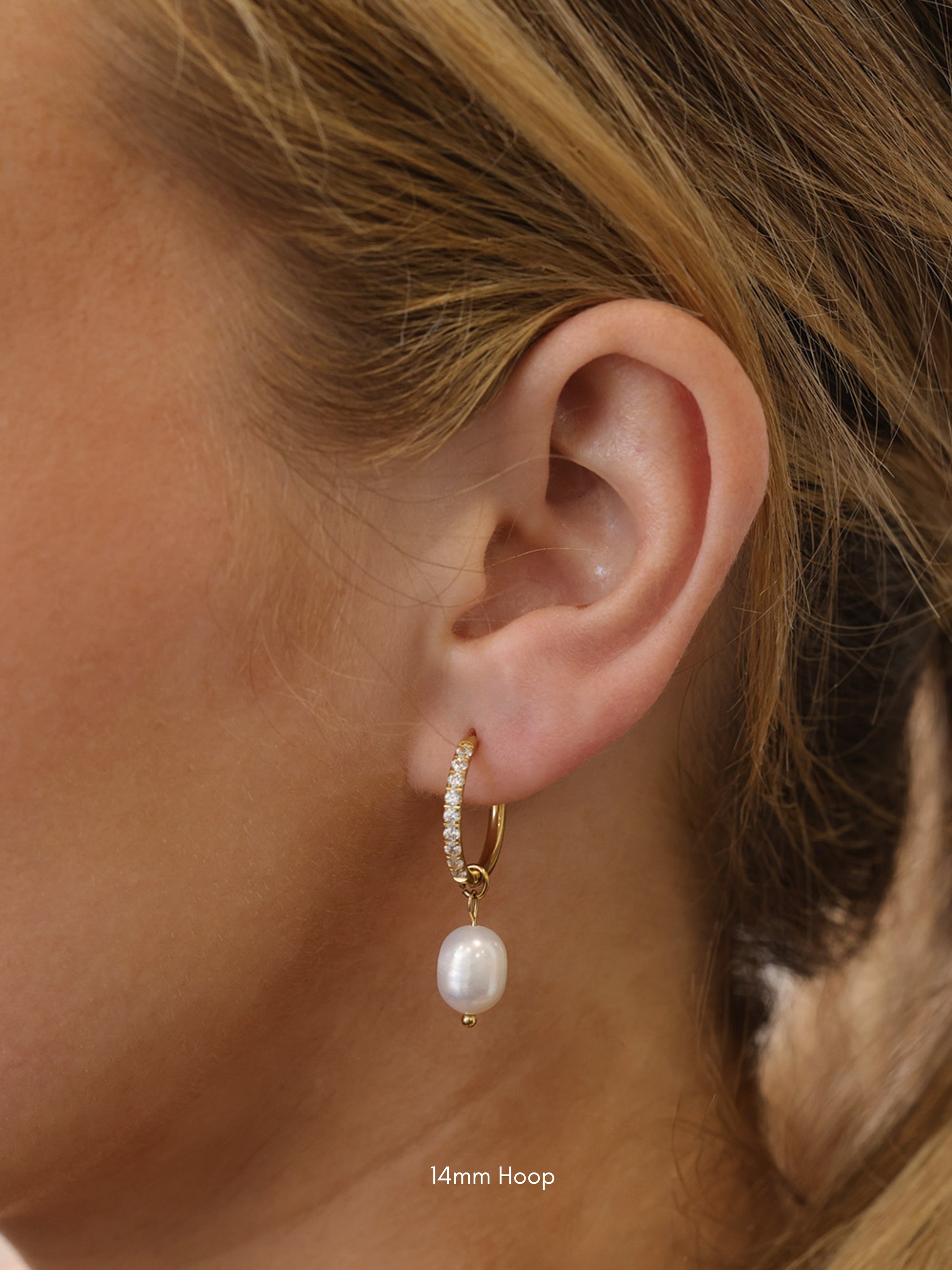 Three sizes of gold pavé waterproof hoop earrings with natural freshwater pearl drops displayed on a textured neutral background