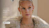 A promotional banner featuring a blonde woman in a beige faux fur coat, wearing gold jewelry including a gold hoop earring and layered gold necklaces. The left side features promotional text for a 'Sitewide Sale' with a 'Shop the Sale' button.