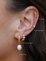 A woman's ear styled with a curated four-piece gold ear stack — a cubic zirconia huggie with baroque pearl drop, a gold floral huggie, a marquise climber and a clover stud.