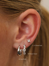 Close-up of a person's ear showing three silver earrings labeled A. Lucy Small, B.