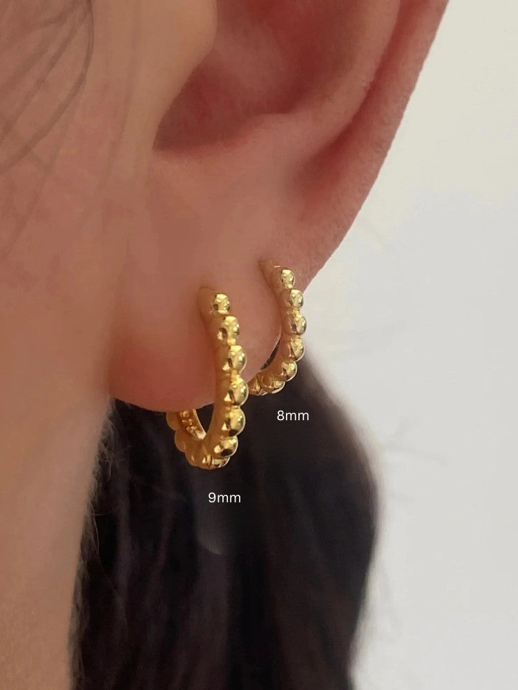 Sterling silver beaded hoop earrings in 8mm and 9mm sizes, featuring polished spherical detailing for a dainty, minimalist look. Displayed on a neutral textured surface with soft floral accents.