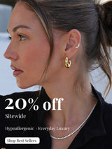   
Side‑profile close‑up of a woman wearing gold hoop earrings, a small ear cuff, and a delicate crystal necklace, styled with her hair in a bun and a black collared shirt. Promotional text on the image highlights a 20% sitewide sale and hypoallergenic everyday luxury jewellery.