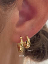 Close-up of a person's ear wearing two small gold hoop earrings with tiny clear stones, labeled Style B and Style C.