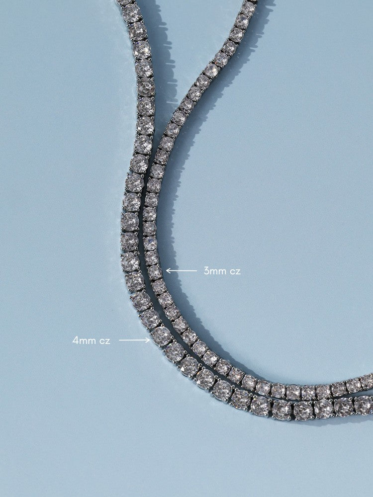 A close-up of a double-row tennis necklace with clear cubic zirconia stones in a silver-toned setting, shown on a light blue background with white text labels indicating 3mm cz and 4mm cz spacing.