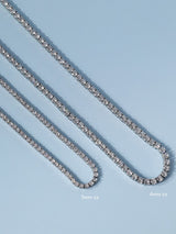 Two silver tennis chains laid diagonally on a light blue background, labelled 3mm and 4mm chain widths.