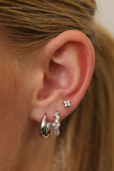 Silver teardrop huggie hoop worn with a pavé cluster huggie and a four-stone flower stud in a three-piece ear stack.